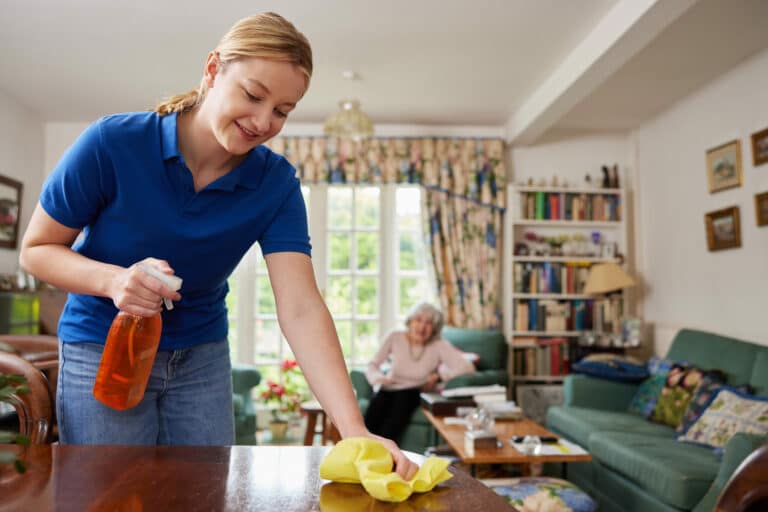 Female Home Help Cleaning House And Talking To Senior Woman